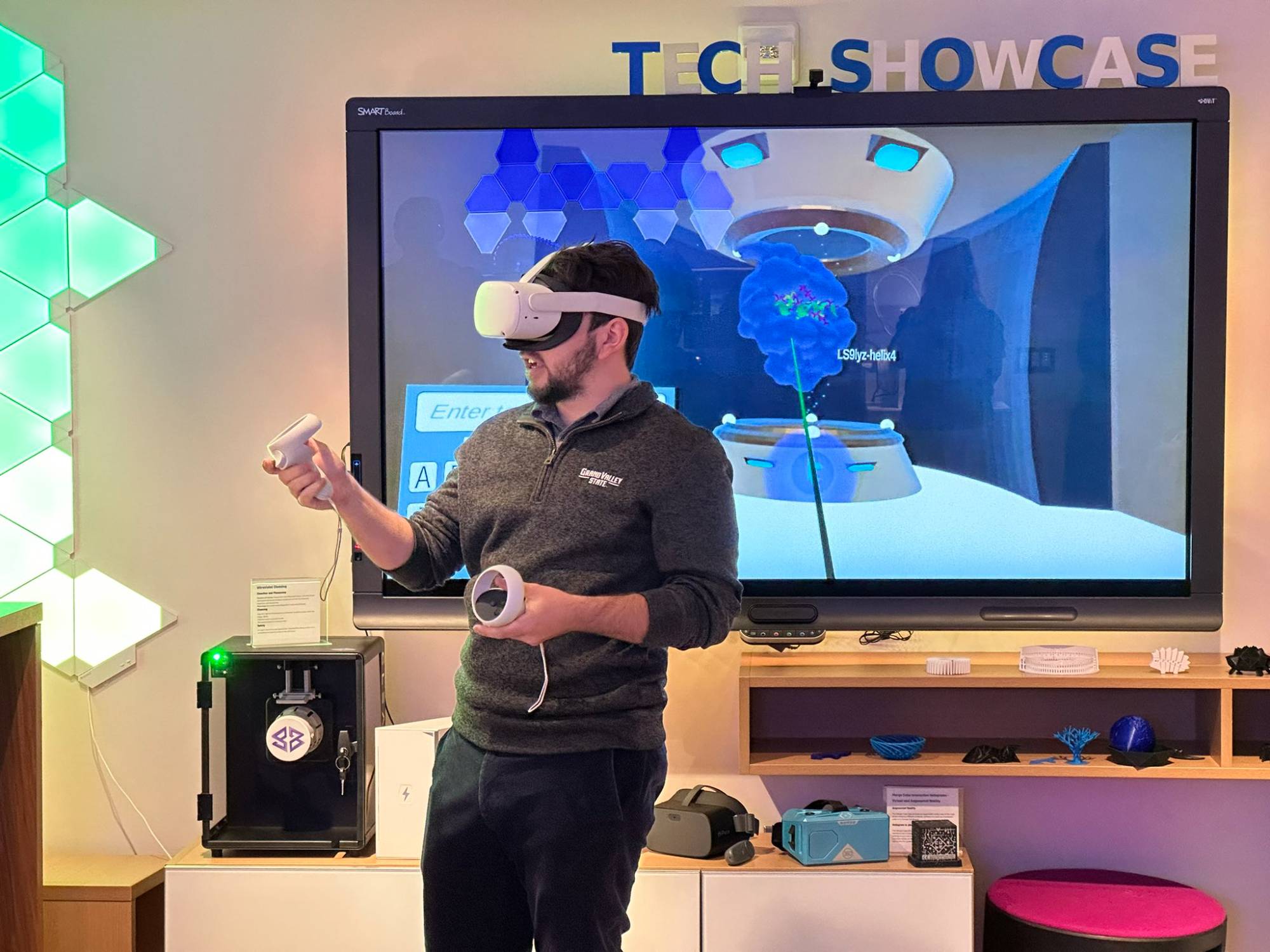 Man in grey shirt and jeans wearing virtual reality headset with large tv screen in the background
